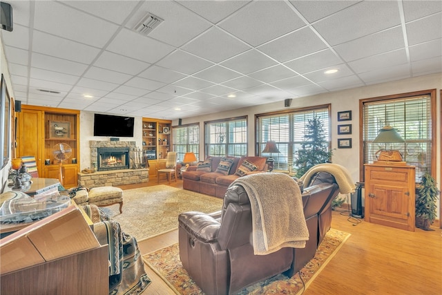 living room with a paneled ceiling, a stone fireplace, and light wood-type flooring