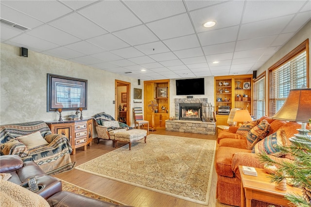 living room with hardwood / wood-style floors, a paneled ceiling, a stone fireplace, and built in shelves