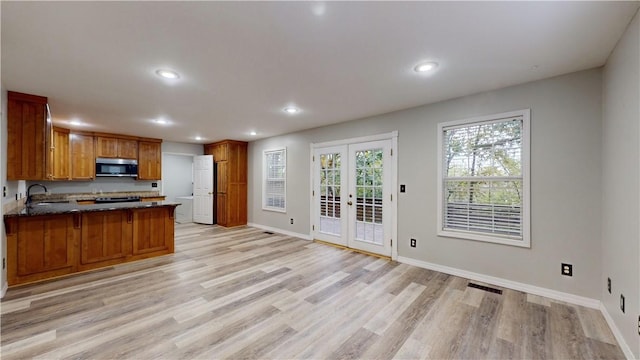 kitchen featuring dark stone countertops, kitchen peninsula, sink, light hardwood / wood-style flooring, and french doors