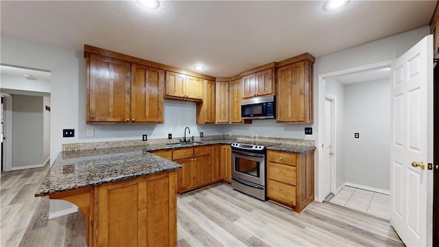 kitchen featuring appliances with stainless steel finishes, dark stone countertops, a kitchen breakfast bar, kitchen peninsula, and light wood-type flooring