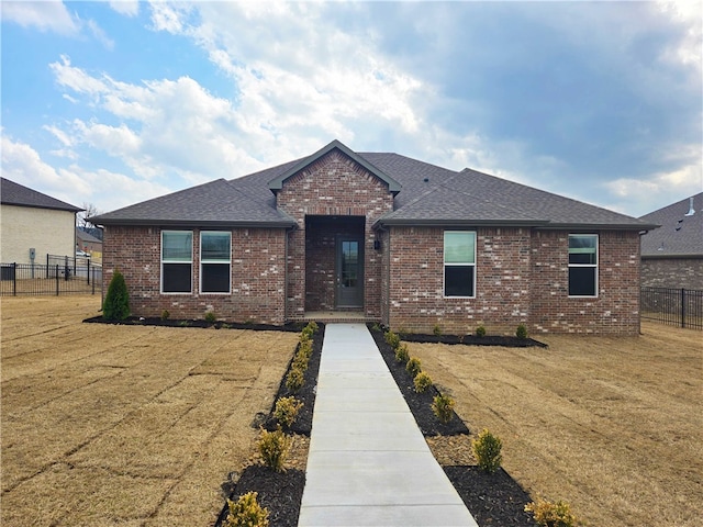 ranch-style house featuring brick siding, a front lawn, fence, and roof with shingles