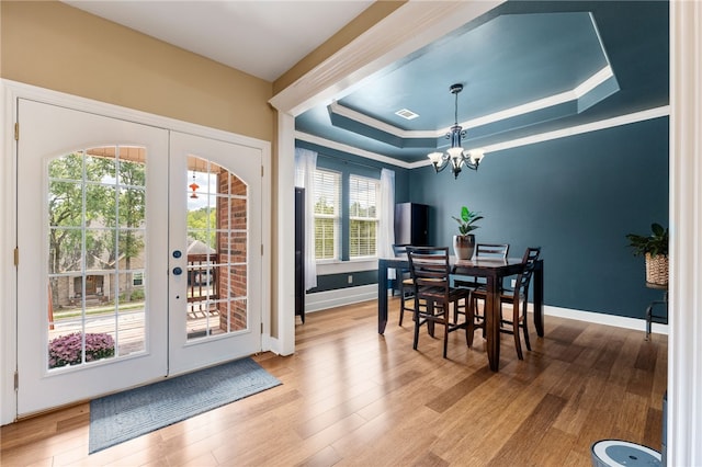 dining space with french doors, hardwood / wood-style flooring, an inviting chandelier, and a raised ceiling