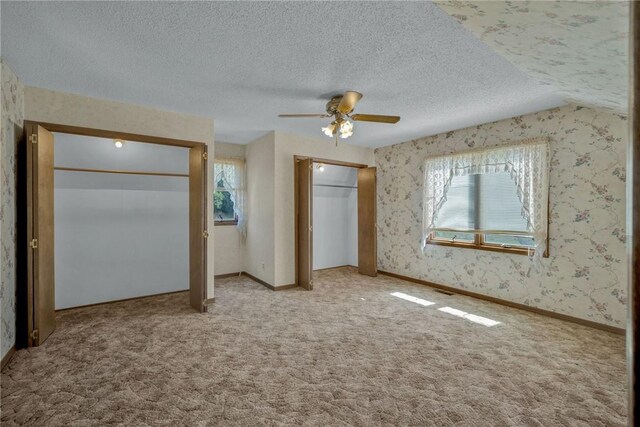 unfurnished bedroom featuring ceiling fan, multiple windows, light carpet, and two closets