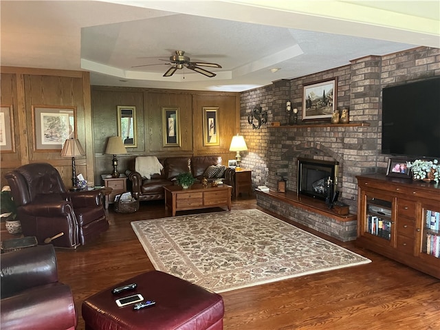 living room with ceiling fan, a fireplace, dark hardwood / wood-style floors, and a raised ceiling