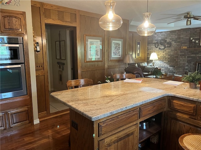 kitchen featuring stainless steel double oven, hanging light fixtures, dark hardwood / wood-style flooring, light stone countertops, and ceiling fan