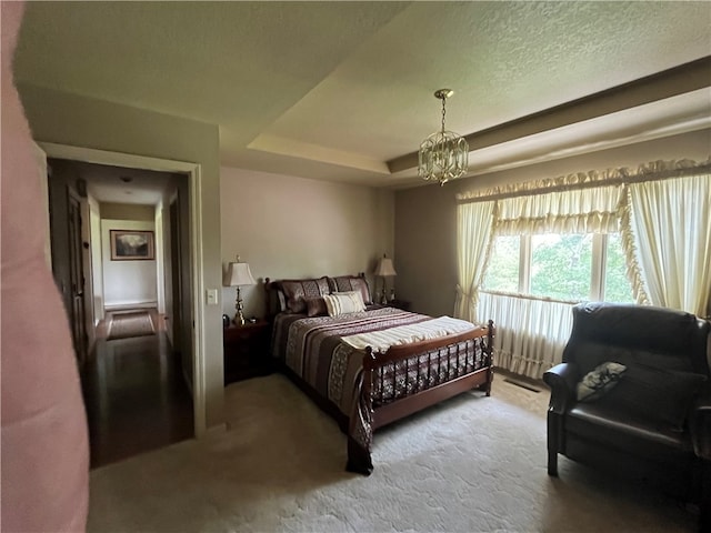 bedroom featuring an inviting chandelier, a tray ceiling, a textured ceiling, and carpet floors