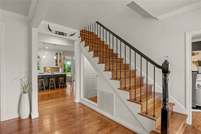 staircase with wood-type flooring and crown molding