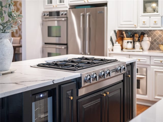 kitchen featuring light wood-type flooring, white cabinets, stainless steel appliances, backsplash, and light stone countertops