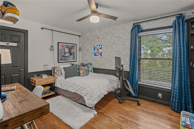 bedroom with hardwood / wood-style floors, ceiling fan, and brick wall