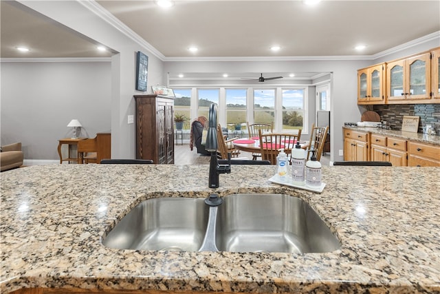 kitchen with light stone countertops, sink, ceiling fan, backsplash, and ornamental molding