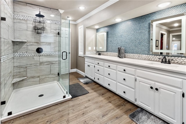 bathroom with backsplash, wood-type flooring, a shower with door, vanity, and ornamental molding