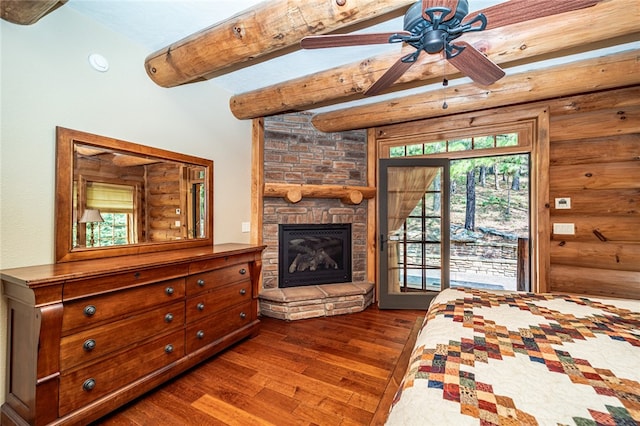 bedroom featuring dark wood-type flooring, a stone fireplace, access to exterior, ceiling fan, and vaulted ceiling with beams