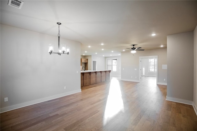 unfurnished living room with light wood-type flooring and ceiling fan with notable chandelier