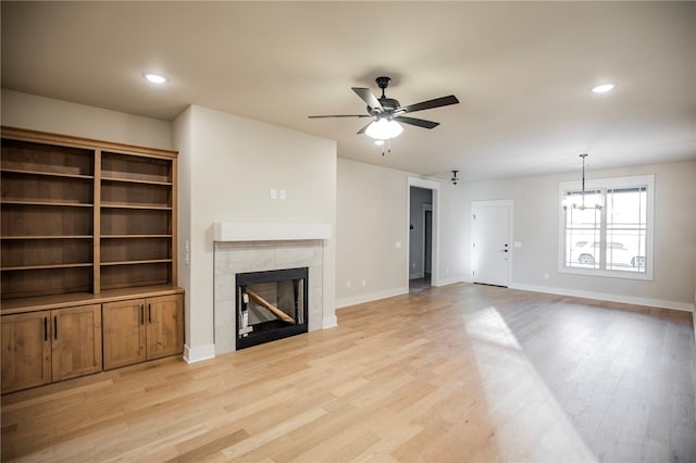 unfurnished living room featuring ceiling fan with notable chandelier, a tile fireplace, and light hardwood / wood-style flooring