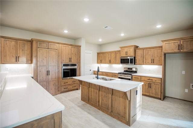 kitchen with a center island with sink, sink, appliances with stainless steel finishes, light stone countertops, and decorative backsplash