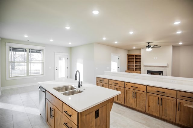 kitchen featuring a center island with sink, sink, stainless steel dishwasher, a tile fireplace, and ceiling fan