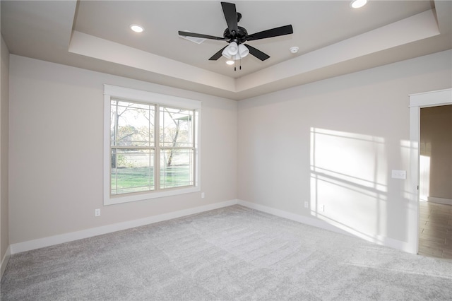 unfurnished room with a tray ceiling, light colored carpet, and ceiling fan