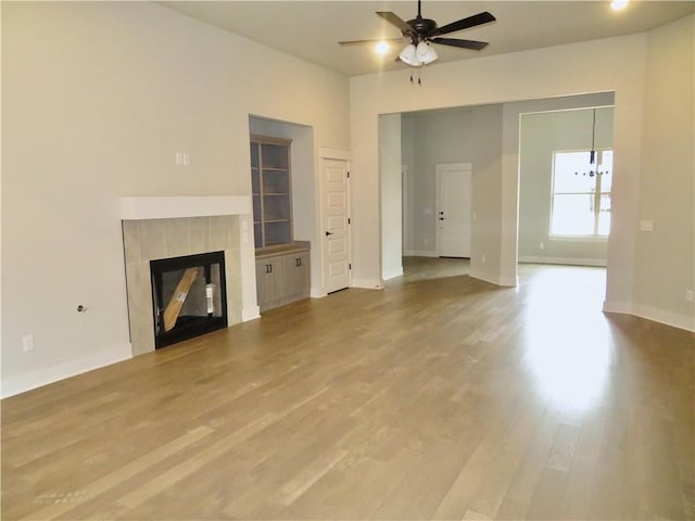 unfurnished living room featuring a tiled fireplace, wood finished floors, baseboards, and ceiling fan