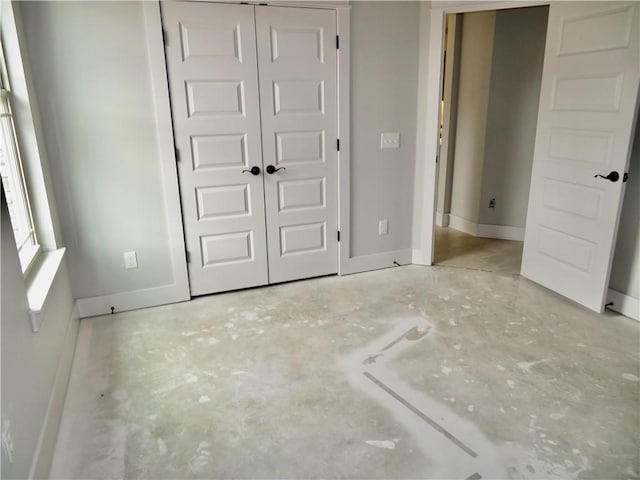 unfurnished bedroom with a closet, baseboards, and concrete flooring