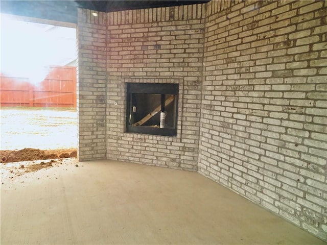 unfurnished living room featuring unfinished concrete flooring, brick wall, and an outdoor brick fireplace