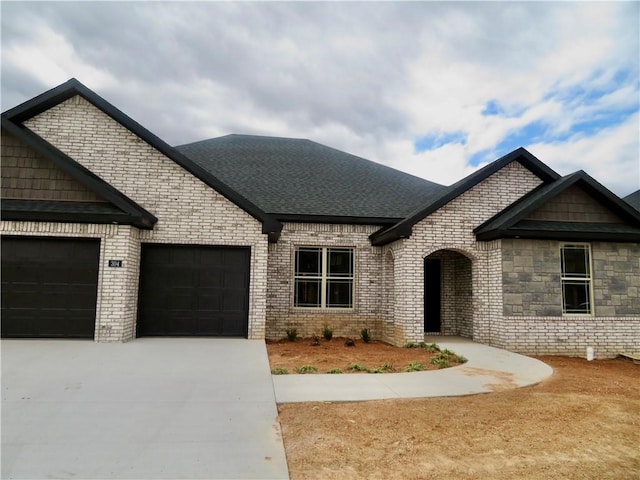 view of front of house featuring an attached garage, brick siding, driveway, and roof with shingles