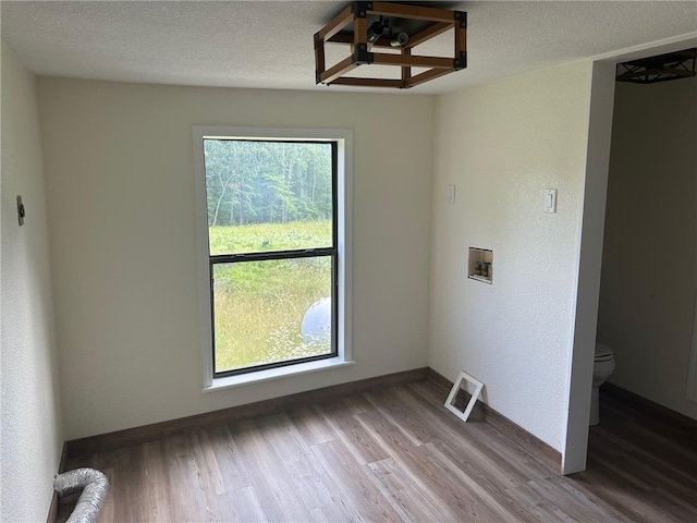 empty room with a textured ceiling, a healthy amount of sunlight, and hardwood / wood-style floors