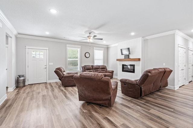 living room with light wood-type flooring, ceiling fan, a fireplace, and crown molding