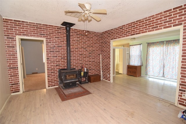 unfurnished living room with a wood stove, a textured ceiling, brick wall, a ceiling fan, and wood finished floors