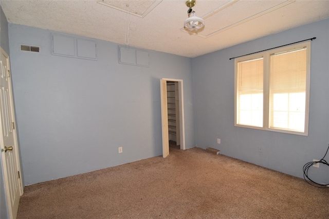 carpeted empty room featuring attic access and visible vents