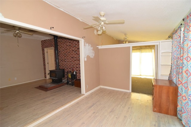 unfurnished living room featuring baseboards, wood finished floors, a ceiling fan, a wood stove, and vaulted ceiling