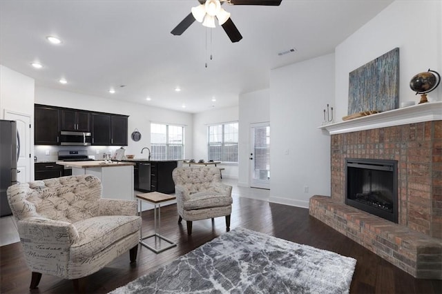 living room featuring sink, dark wood-type flooring, and a brick fireplace