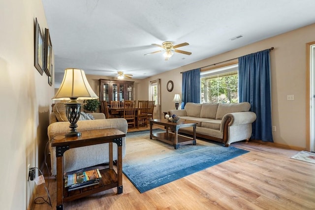 living room featuring a ceiling fan, baseboards, visible vents, and light wood finished floors