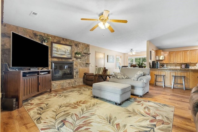 living room with a glass covered fireplace, ceiling fan, light wood-type flooring, and visible vents