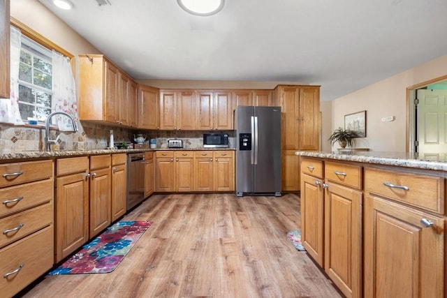 kitchen featuring backsplash, appliances with stainless steel finishes, a sink, light stone counters, and light wood-style flooring