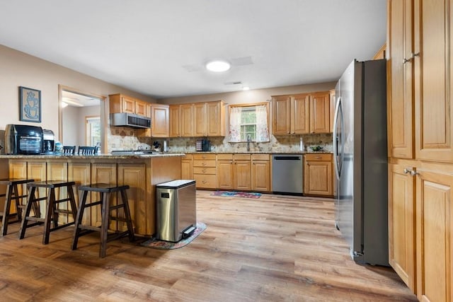 kitchen with light wood-style floors, a kitchen breakfast bar, stainless steel appliances, and tasteful backsplash