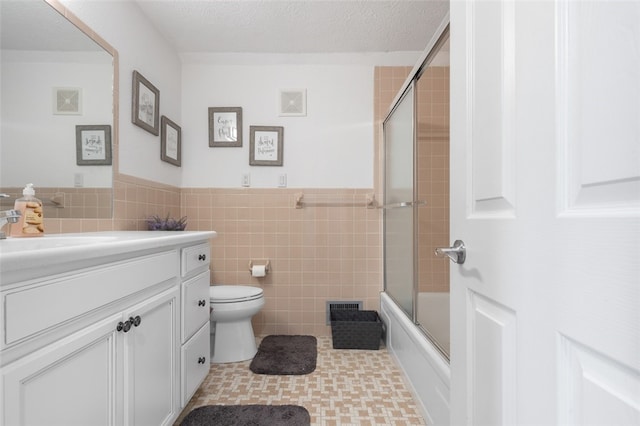 full bathroom with tile walls, bath / shower combo with glass door, vanity, and toilet