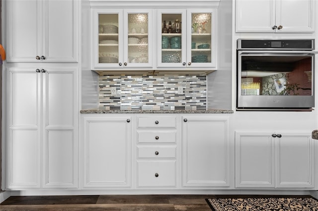 bar with dark stone countertops, white cabinets, backsplash, and oven