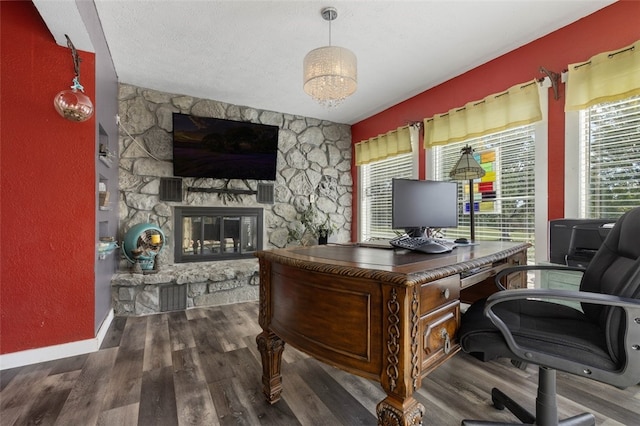 home office with a stone fireplace, a textured ceiling, and dark wood-type flooring