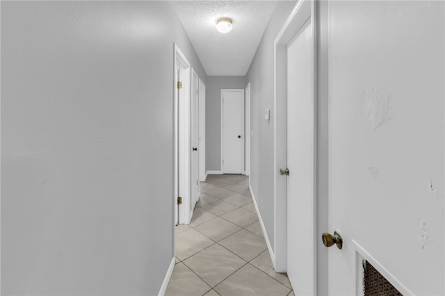 hallway with a textured ceiling and light tile patterned floors