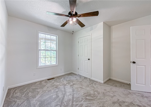 unfurnished bedroom featuring a textured ceiling, ceiling fan, light colored carpet, and a closet