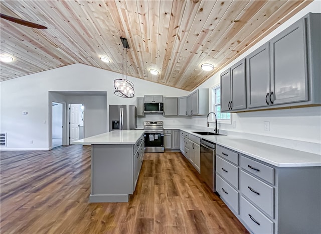 kitchen with appliances with stainless steel finishes, gray cabinetry, vaulted ceiling, a kitchen island, and sink