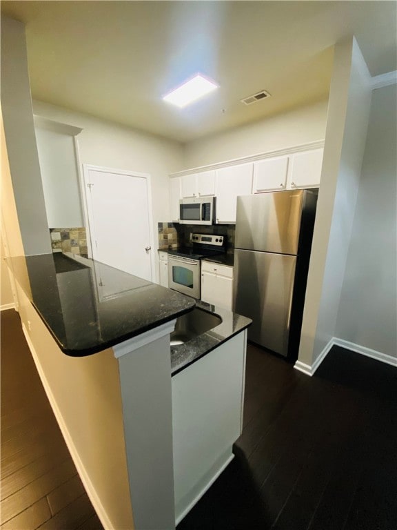 kitchen featuring kitchen peninsula, dark hardwood / wood-style floors, tasteful backsplash, white cabinets, and appliances with stainless steel finishes