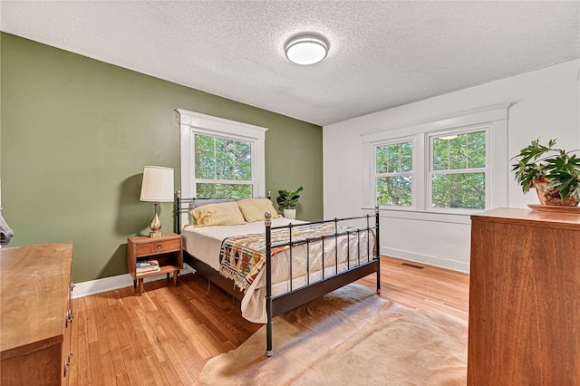 bedroom with multiple windows, a textured ceiling, and light hardwood / wood-style flooring