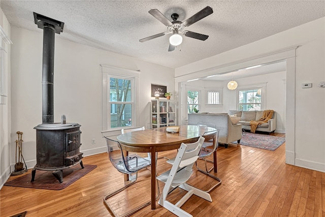 dining space featuring a wood stove, light wood-type flooring, ceiling fan, and a textured ceiling