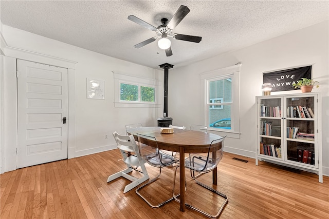 dining room featuring a wood stove, light wood-type flooring, ceiling fan, and a textured ceiling