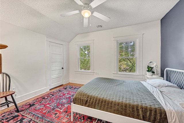 bedroom with a textured ceiling, lofted ceiling, ceiling fan, and hardwood / wood-style flooring