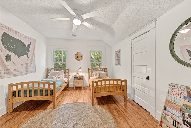 bedroom featuring light hardwood / wood-style flooring, vaulted ceiling, ceiling fan, and a textured ceiling