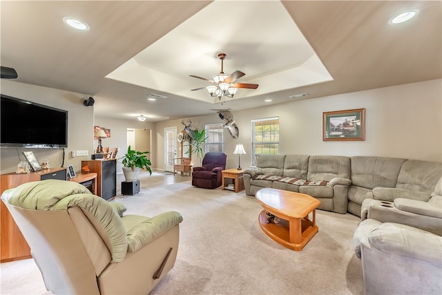 living room with ceiling fan, light colored carpet, and a tray ceiling