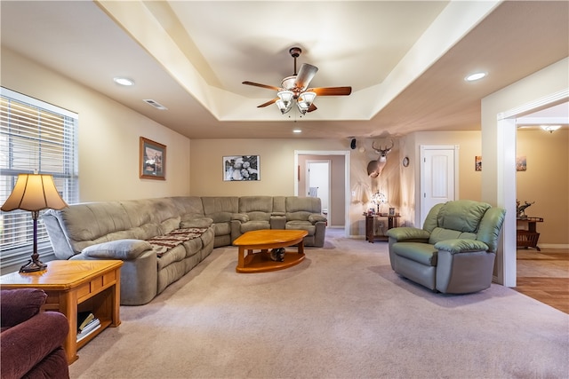 carpeted living room with a tray ceiling and ceiling fan