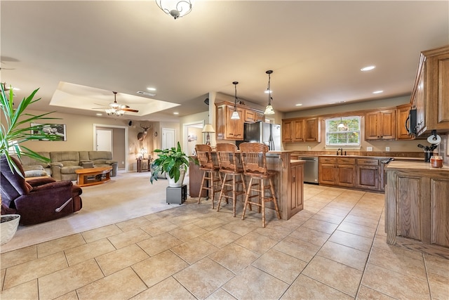 kitchen with a breakfast bar, pendant lighting, a tray ceiling, stainless steel appliances, and ceiling fan